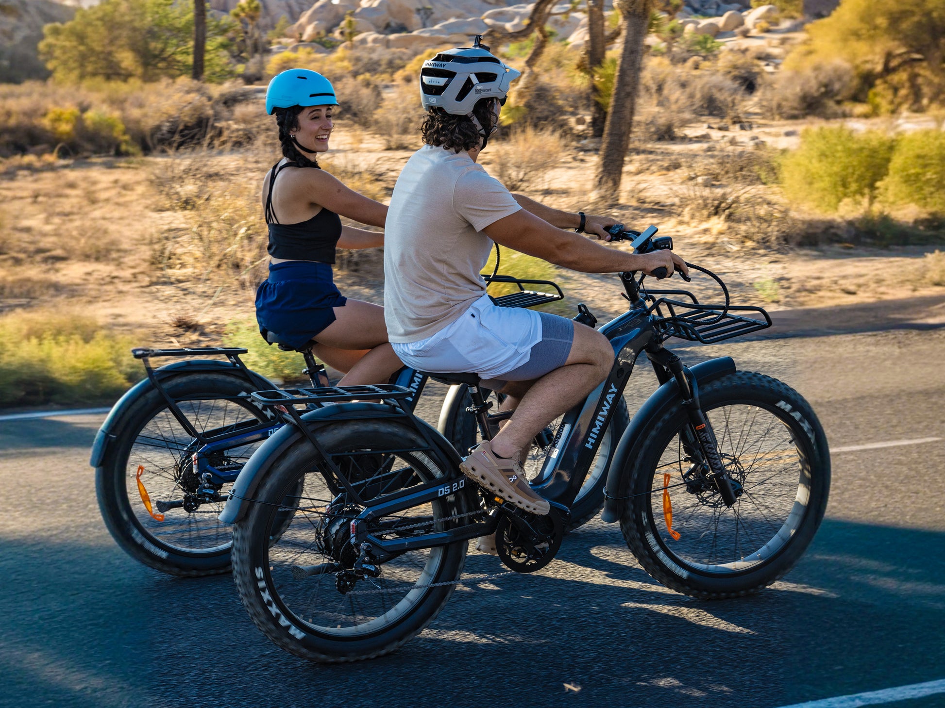 Two riders cycling side-by-side on a paved desert road on Himiway D5 2.0 full suspension fat tire electric bikes.