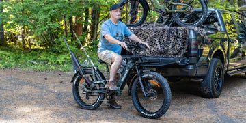 A fisherman sitting on the Himiway D5 2.0 camo fat tire electric bike equipped with a fishing rod holder next to a pickup truck.