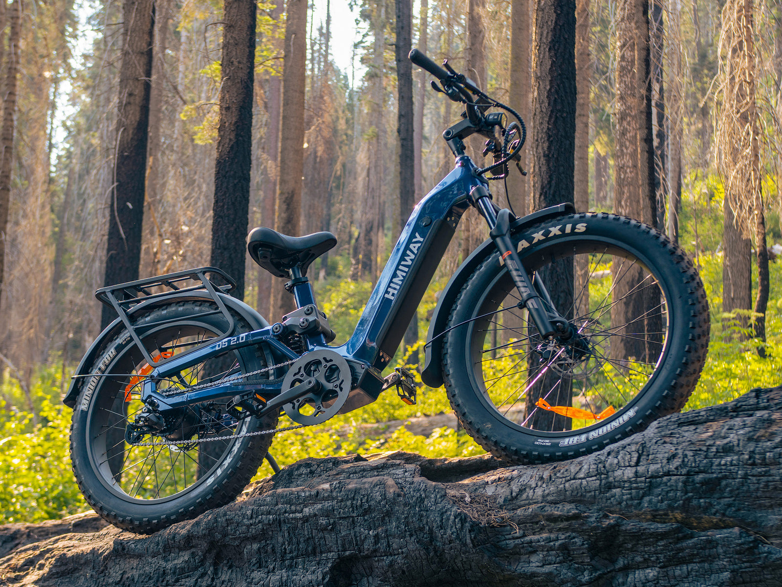 A Midnight Blue Himiway D5 2.0 step-thru fat tire electric bike parked on a large fallen log in a dense forest.
