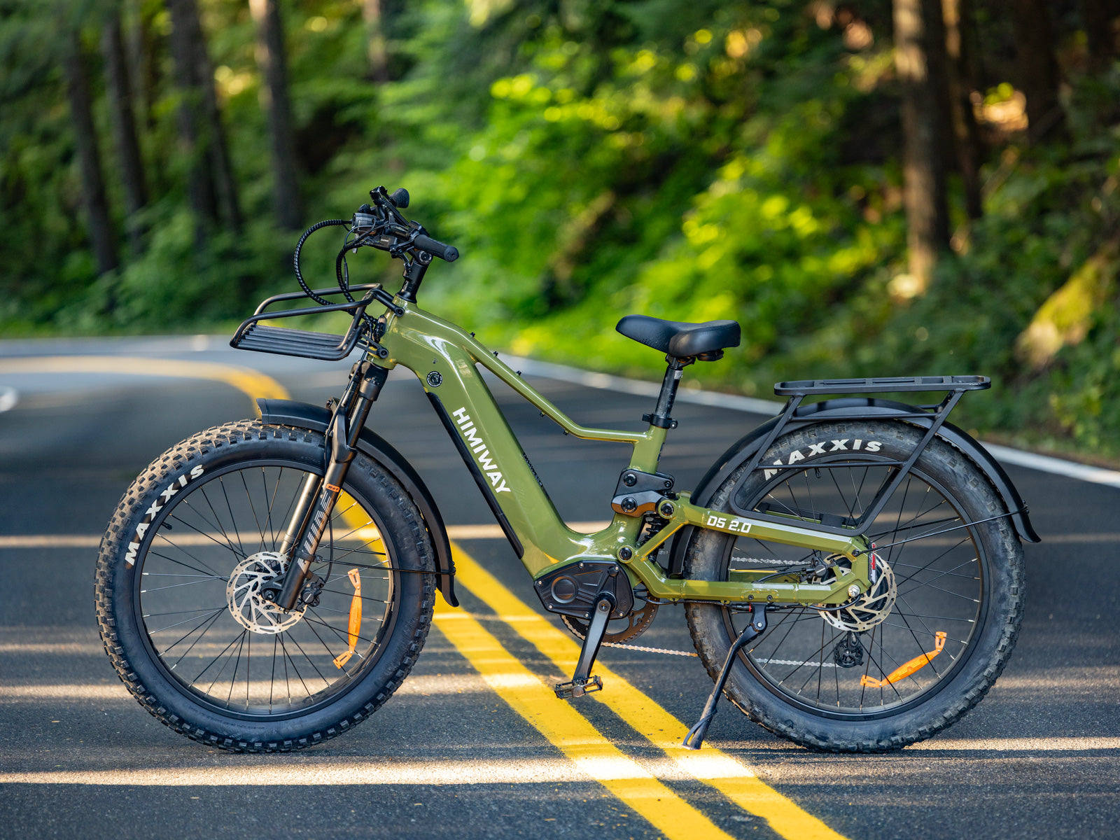 The olive green Himiway D5 2.0 step-thru fat tire electric bike parked on a scenic paved forest road.