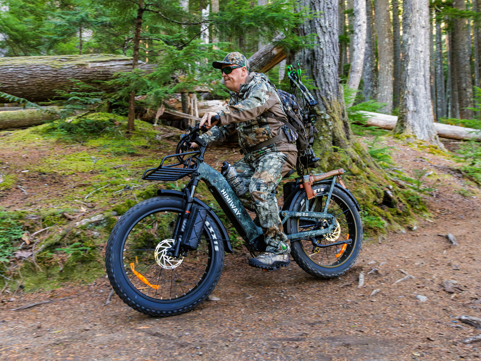 A bowhunter in full camouflage riding the Himiway D5 2.0 camo full suspension fat tire electric bike on a dense forest trail.