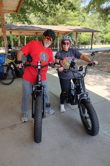 Himiway D5 2.0 electric bike carrying a senior couple smiling at the camera under a garden shelter with trees in the background