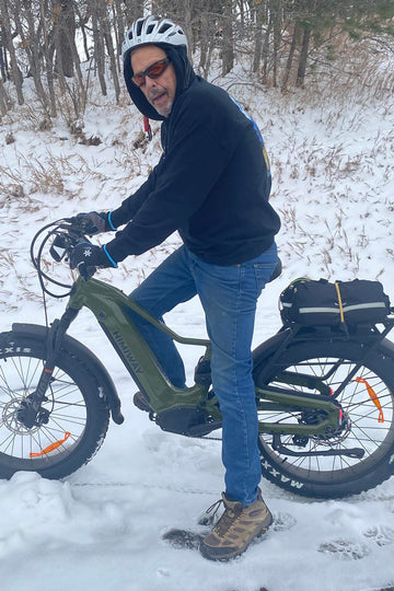Himiway D5 2.0 Olive Green electric bike ridden by a helmeted senior rider standing on snowy terrain with bare trees in the background