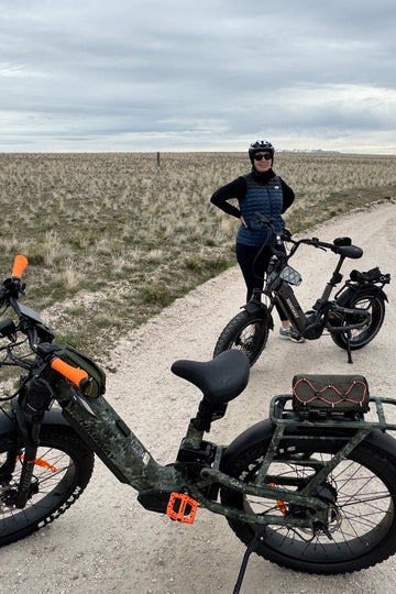 A woman cyclist taking a break with two Himiway step-thru fat tire e-bikes, including a camo model, on a gravel trail.