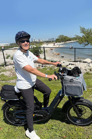 Man riding an himiway D5 2.0 st ebike with a dog in a basket near a beach.